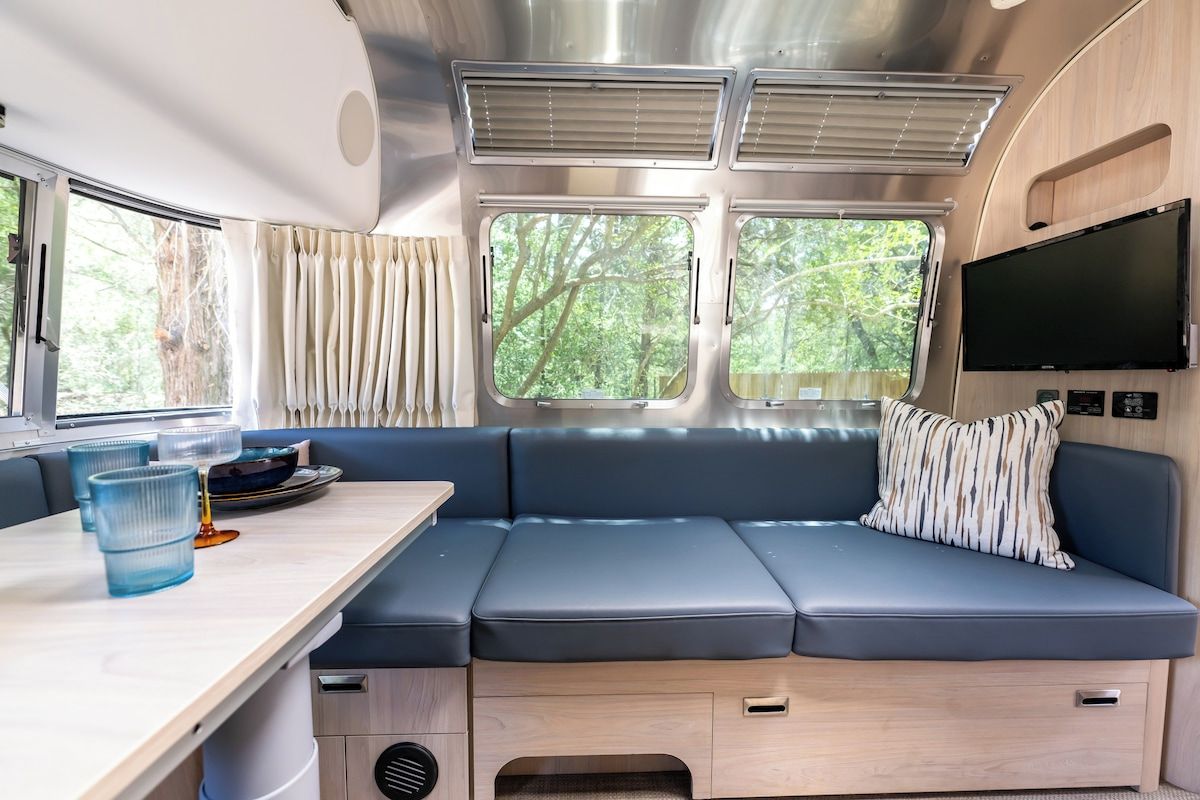 Un interior de autocaravana moderna con un sofá, una mesa de comedor y un televisor montado en la pared.