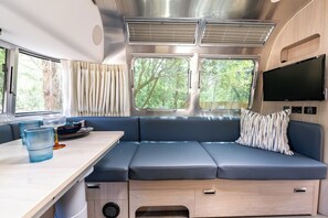 Ein modernes Wohnmobil-Interieur mit einer Sitzecke, einem Esstisch und einem an der Wand befestigten Fernseher.