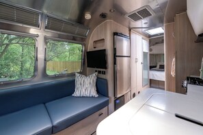 Ein kompaktes Wohnmobil-Interieur mit einer Küchenzeile, einer Sitzecke mit gepolsterten Bänken und einem kleinen Fernseher.