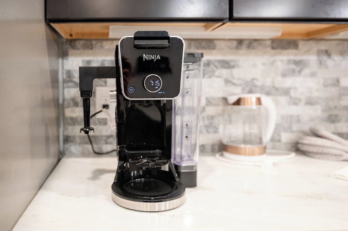 A coffee maker with a digital display, a transparent water carafe, and a white mug on a kitchen counter.
