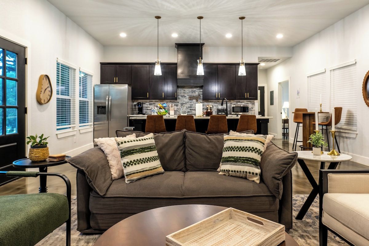 A modern living room with a dark brown sofa, a coffee table, and a kitchen area in the background.