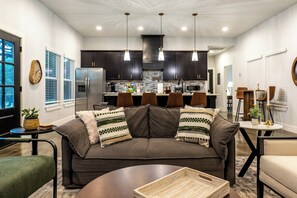 A modern living room with a dark brown sofa, a coffee table, and a kitchen area in the background. - Modern Hilltop Farmhouse w/Patio in Wine Country (Fredericksburg)