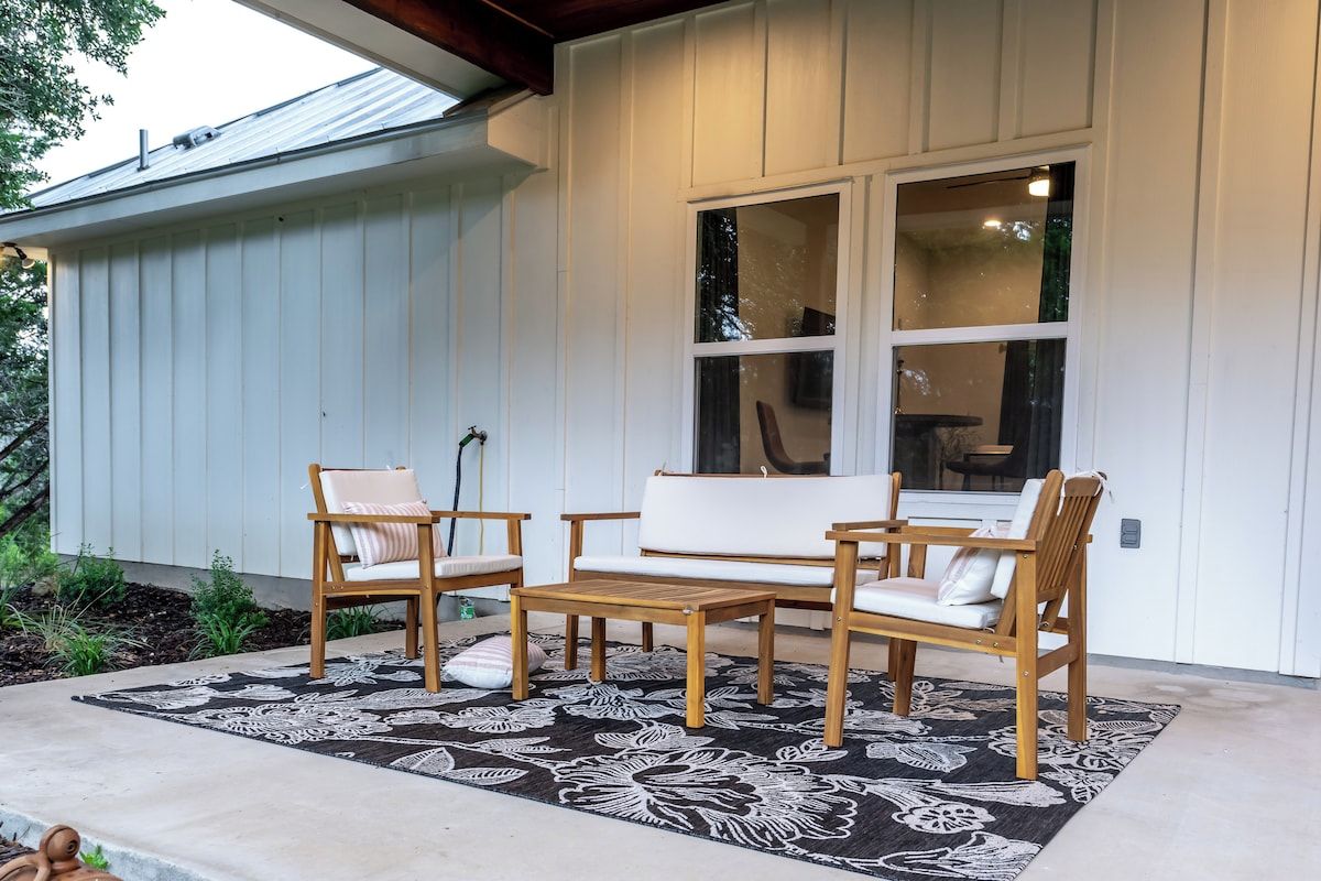 Un patio con una mesa y sillas de madera, un tapete estampado y una ventana que ofrece vistas del interior.