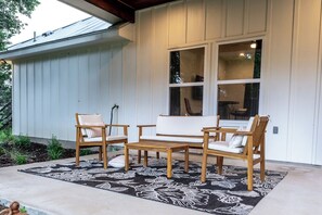 A patio with a wooden table and chairs, a patterned rug, and a window with a view of the interior. - Modern Hilltop Farmhouse w/Patio in Wine Country (Fredericksburg)