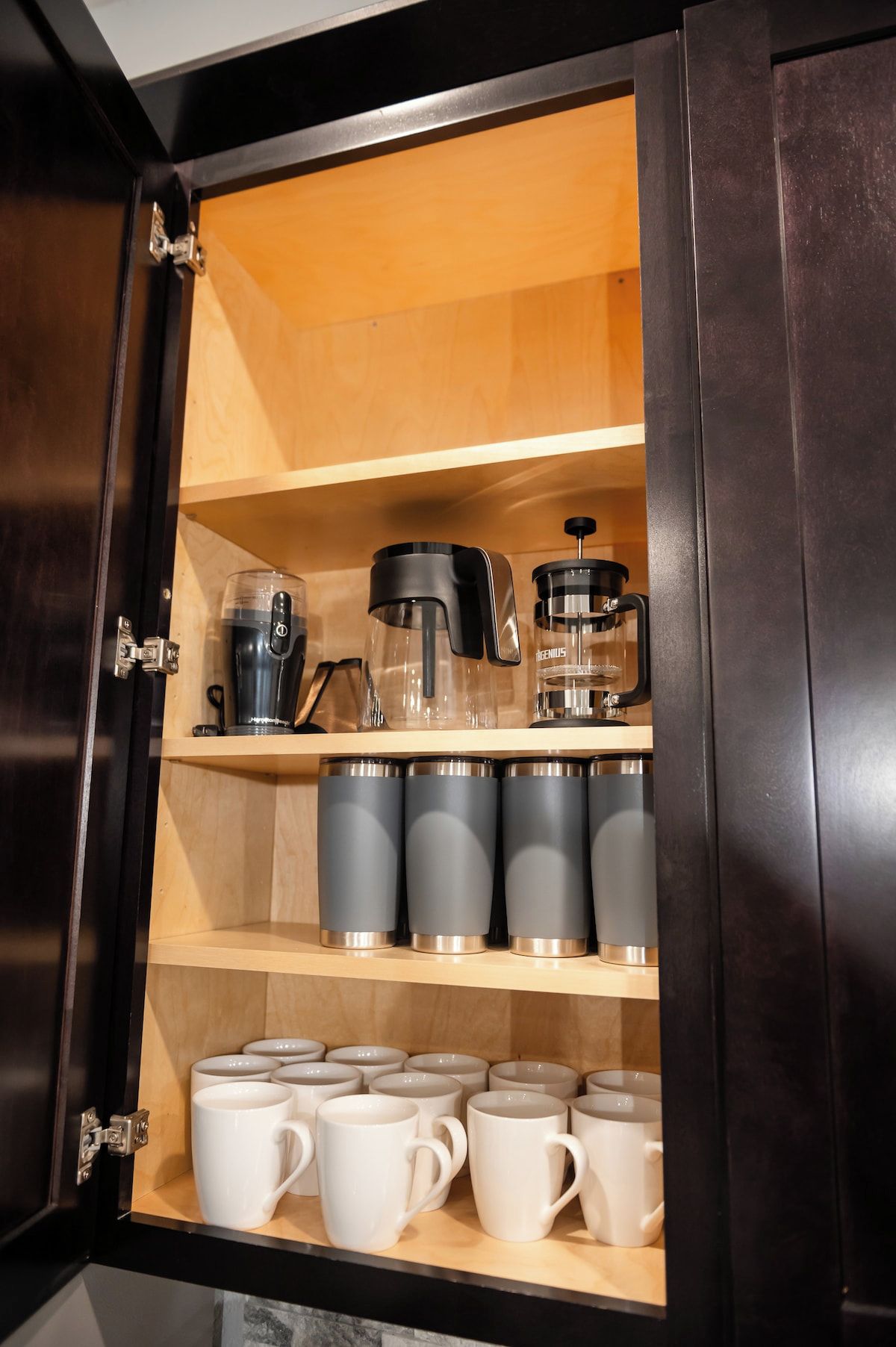 A kitchen cabinet with a coffee maker, a grinder, and multiple mugs.