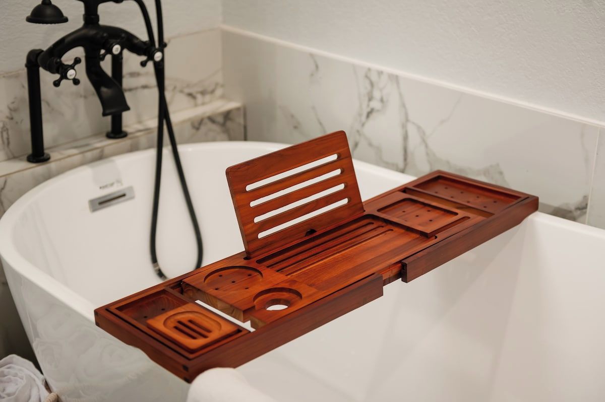 Un baño con una bañera blanca, una bandeja de madera con divisiones y un grifo negro.