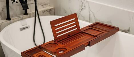 Un baño con una bañera blanca, una bandeja de madera con divisiones y un grifo negro.