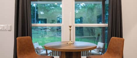 Una mesa de madera redonda con dos sillas, una vela y una ventana con cortinas.