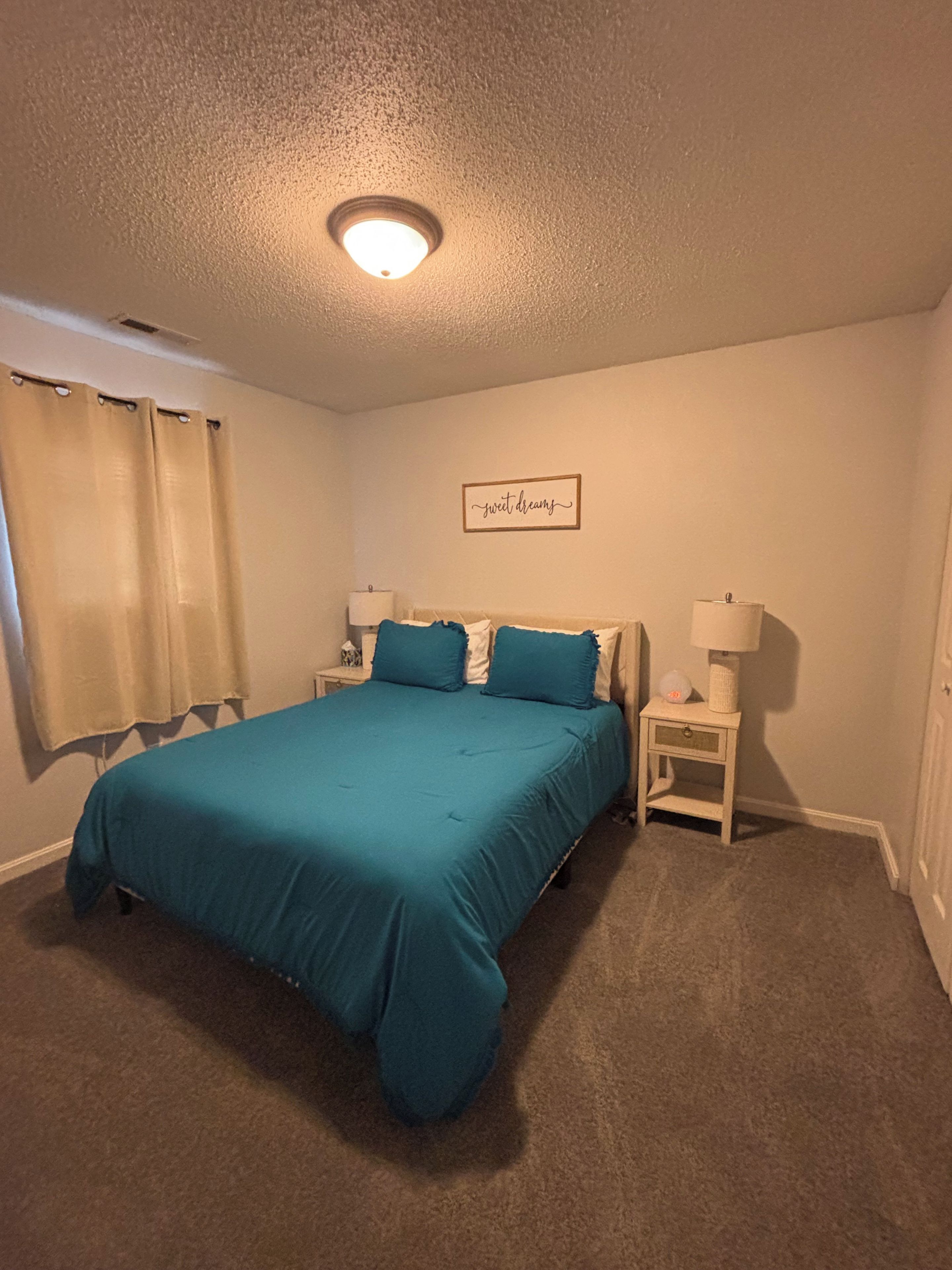 A bedroom with a single bed, a nightstand, a lamp, a wall clock, and a ceiling light.