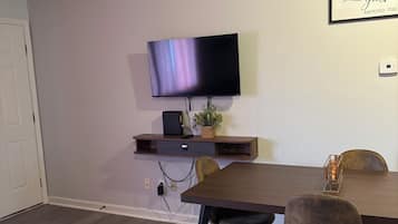A modern dining area with a flat-screen TV mounted on the wall, a wooden table, and two chairs.