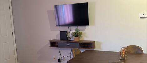 A modern dining area with a flat-screen TV mounted on the wall, a wooden table, and two chairs.