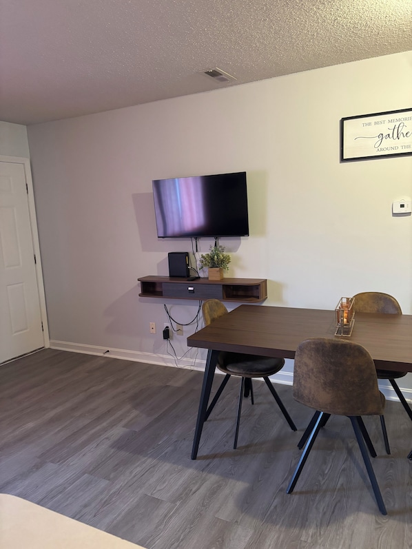 A modern dining area with a flat-screen TV mounted on the wall, a wooden table, and two chairs.