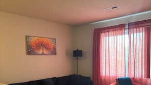Een woonkamer met een donkere bank, een klein tafeltje, een rode fauteuil, een kamerkleed met dessin en een schilderij aan de muur.