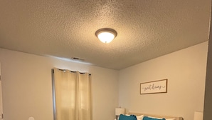 Een slaapkamer met een bed, een nachtkastje, een wandlamp, een raam met gordijnen en een plafondlamp.
