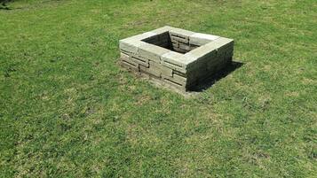 A square stone structure with a central opening, surrounded by grass.