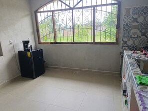 A room with a large window, a black refrigerator, and a tiled floor.