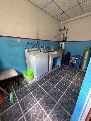 A compact laundry room with a washing machine, a sink, and a drying rack.