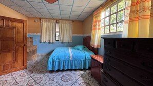 A bedroom with a bed, a dresser, a window with curtains, and a patterned floor.