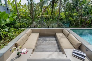 A poolside seating area with a built-in sofa, a small table with a book and a potted plant, and a clear view of the pool. - Basic House (Gianyar)