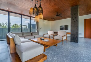 A modern living room with a sectional sofa, two armchairs, a coffee table, and a ceiling fan. - Basic House (Gianyar)