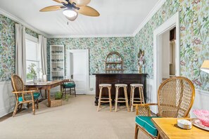 Quarto com mesa de jantar, cadeiras, área de bar e ventilador de teto.