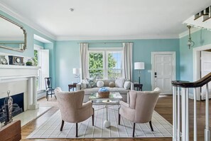 Sala de estar com lareira, um sofá, duas poltronas, uma mesa de centro e uma escada.