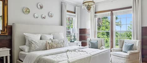 Un dormitorio con una cama grande, una silla, una mesita de noche y una araña.
