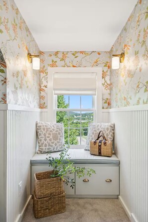 A corner room with a window, a bench with cushions, a basket, and a wall-mounted light fixture. - The Pearl Retreat (Nashville)