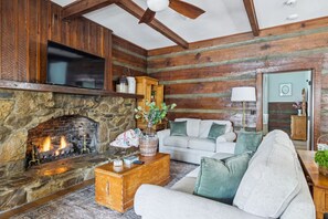 A cozy living room with a stone fireplace, wooden walls, a flat-screen TV, a white sofa, and a ceiling fan. - The Pearl Retreat (Nashville)
