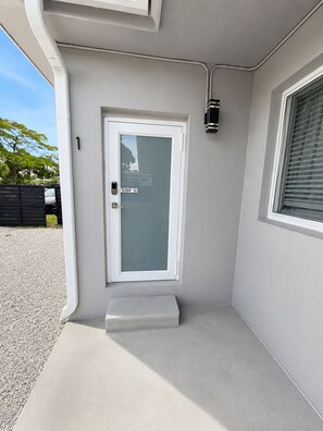 A modern entrance with a glass door, a small step leading to a concrete floor, and a window with blinds. - King Retreat with Pool near Miami Beach (Miami)