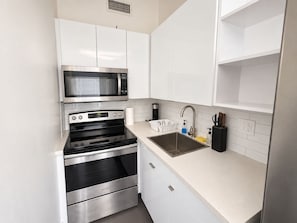 A compact kitchen with white cabinets, a stainless steel microwave, an oven, and a sink. - King Retreat with Pool near Miami Beach (Miami)