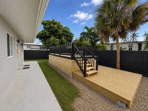 A modern outdoor deck with a wooden staircase leading to a raised platform, surrounded by a black fence and palm trees. - King Retreat with Pool near Miami Beach (Miami)