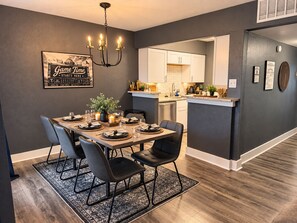 A dining area with a chandelier, a framed sign, and a kitchen in the background. - Destino Stadium Suite 428 (Arlington)