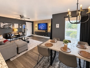 A modern living room with a dining area, a ceiling fan, a flat-screen TV, and a chandelier. - Destino Stadium Suite 428 (Arlington)