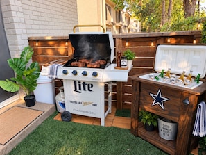 Un barbecue d’extérieur doté d’un compartiment réfrigéré pour les boissons et d’une enseigne décorative.