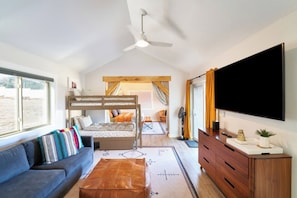 Un soggiorno moderno con un divano, un letto a castello, una TV a schermo piatto e una ventola a soffitto.
