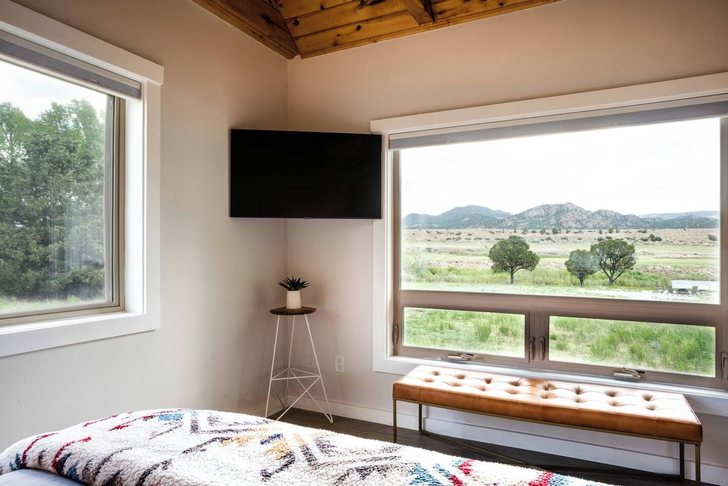 Ein Schlafzimmer mit einem Bett, einer Bank, einem Fernseher und einem Fenster mit Landschaftsblick.
