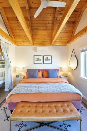 A bedroom with a bed, bedside tables, a bench, a ceiling fan, and framed pictures on the wall.
