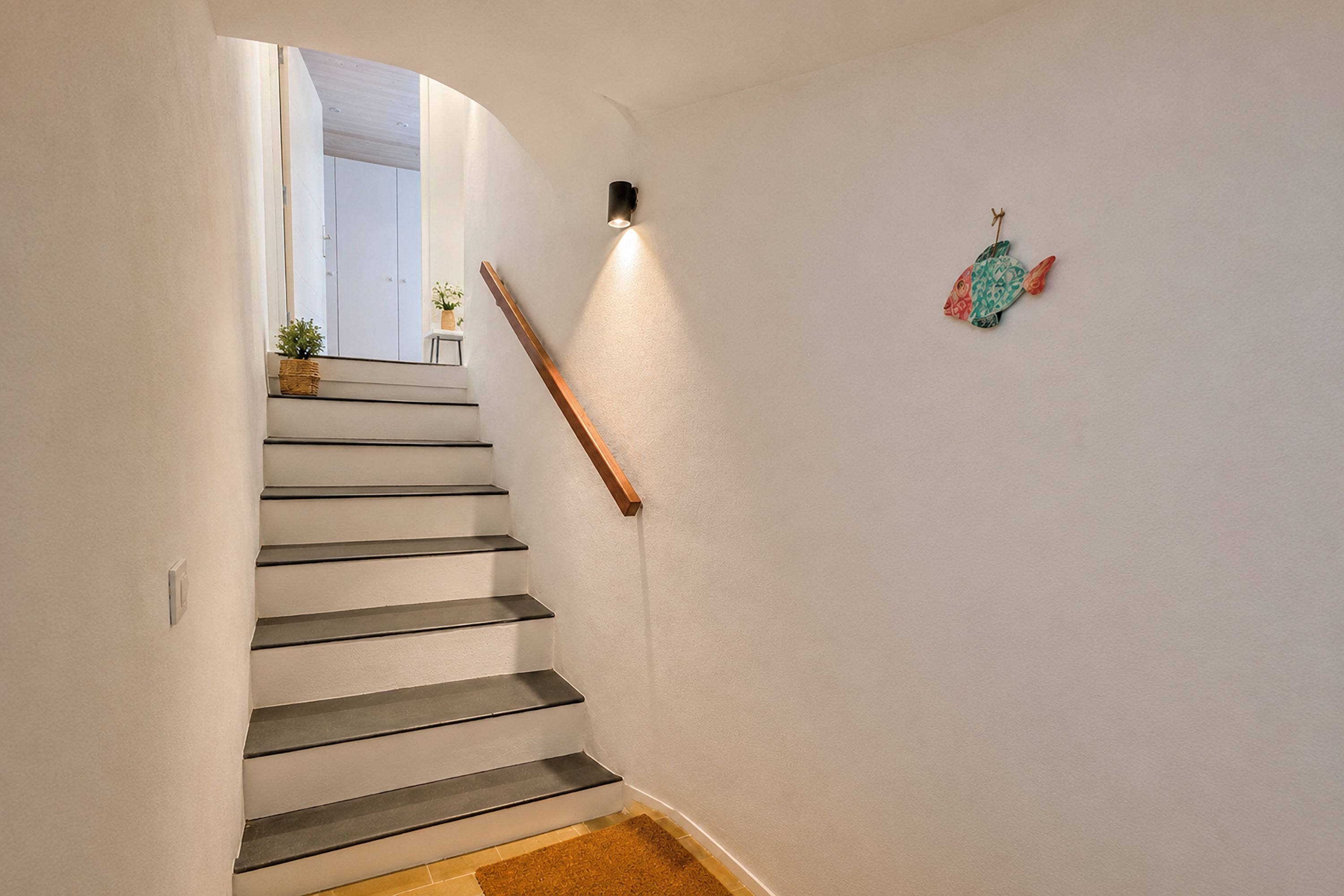 A staircase with a handrail, a wall-mounted light, and a decorative fish ornament.