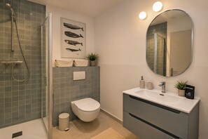 Ein modernes Badezimmer mit Duschkabine aus Glas, Toilette, Waschbecken mit Spiegel und einem gerahmten Bild von Delfinen an der Wand.