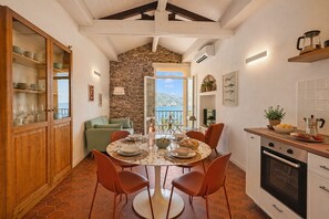 Uma sala de jantar com parede de pedra, vista para o mar e cozinha com fogão.