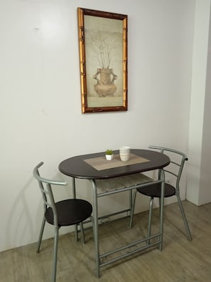 A dining area with a round table, two chairs, a small potted plant, and a framed artwork on the wall.