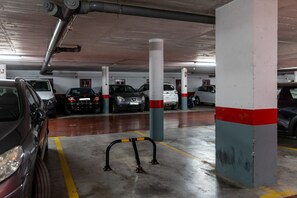 A multi-level parking garage with cars parked in designated spaces, concrete pillars with red and white stripes, and a yellow safety line on the floor. - Manilva Beachfront Promenade by Libehomes (San Luis De Sabinillas)