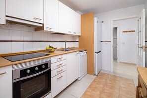 A modern kitchen with white cabinetry, a black stove, and a wooden countertop. - Manilva Beachfront Promenade by Libehomes (San Luis De Sabinillas)
