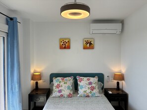 A bedroom with a bed, two nightstands, a ceiling light, two wall-mounted air conditioning units, and a window with a blue curtain. - Manilva Beachfront Promenade by Libehomes (San Luis De Sabinillas)