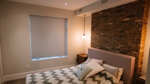 Un dormitorio con una cama, una mesita de noche, una ventana con persianas y una pared de ladrillo decorativa.