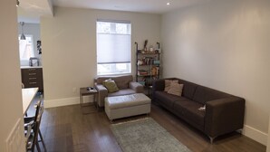 Una sala moderna con un sofá marrón, un sillón blanco, una mesita y una estantería.