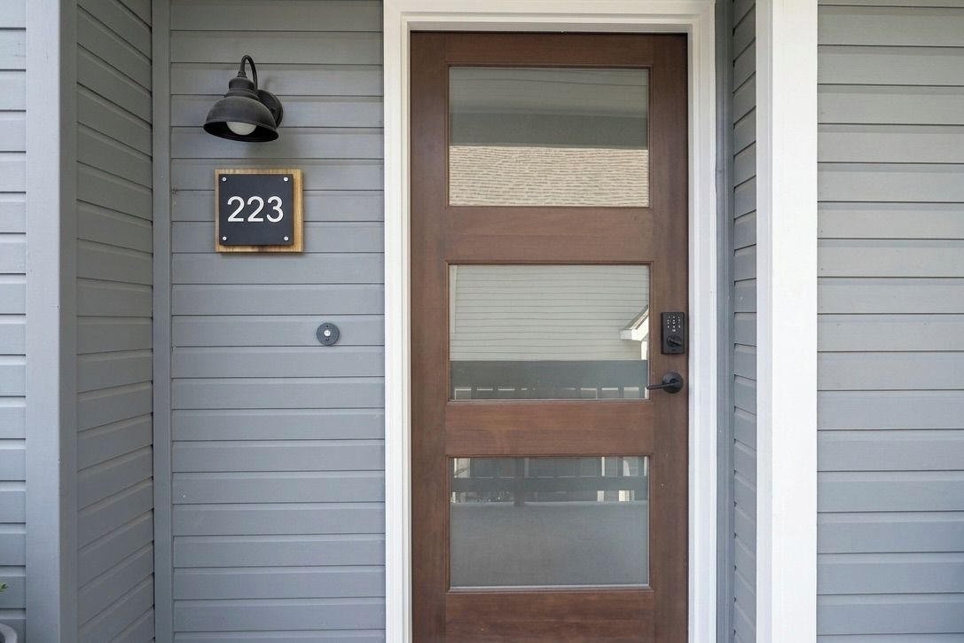 A house number 223, a wooden door with a glass panel, and a wall-mounted light fixture.