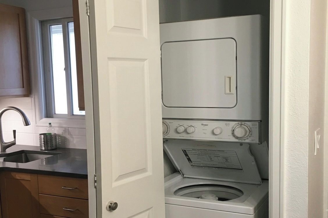 A compact laundry room with a washing machine and dryer, a sink, and wooden cabinets.