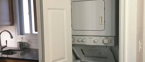 A compact laundry room with a washing machine and dryer, a sink, and wooden cabinets.
